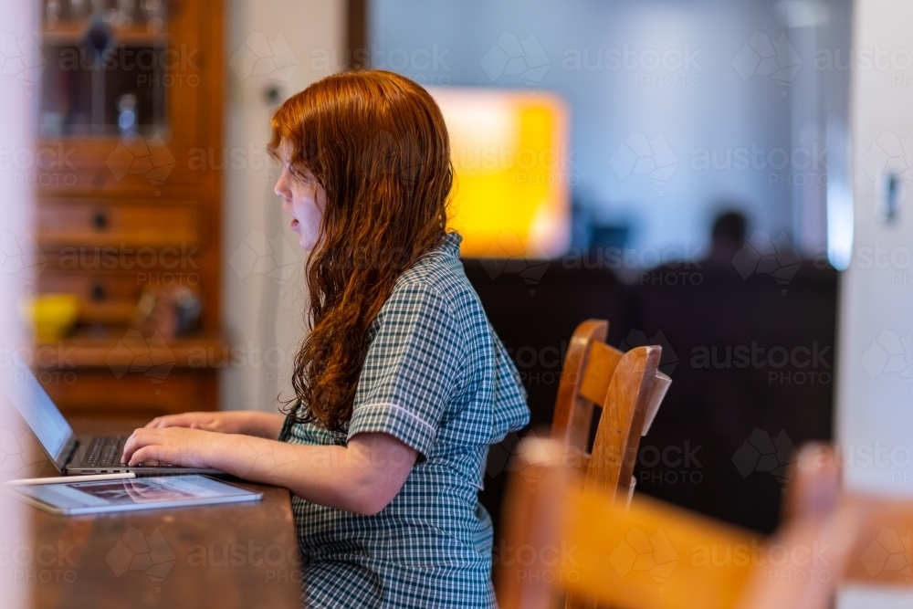 child in school uniform sitting at kitchen bench working on laptop computer - Australian Stock Image