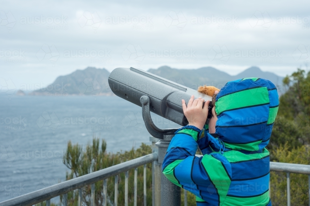 Child looking through binoculars at cliffs and ocean - Australian Stock Image