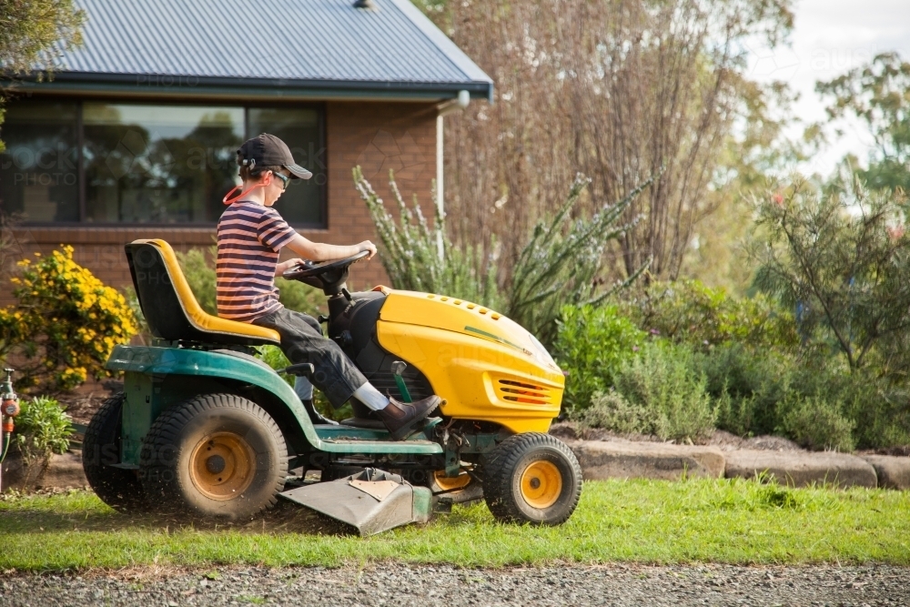 Child mowing the front yard on a ride on lawn mower - Australian Stock Image