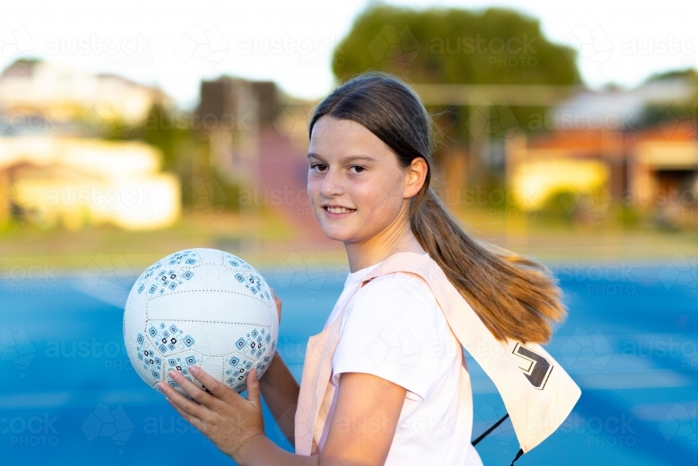 child netball player in action with netball on blue outdoor court - Australian Stock Image