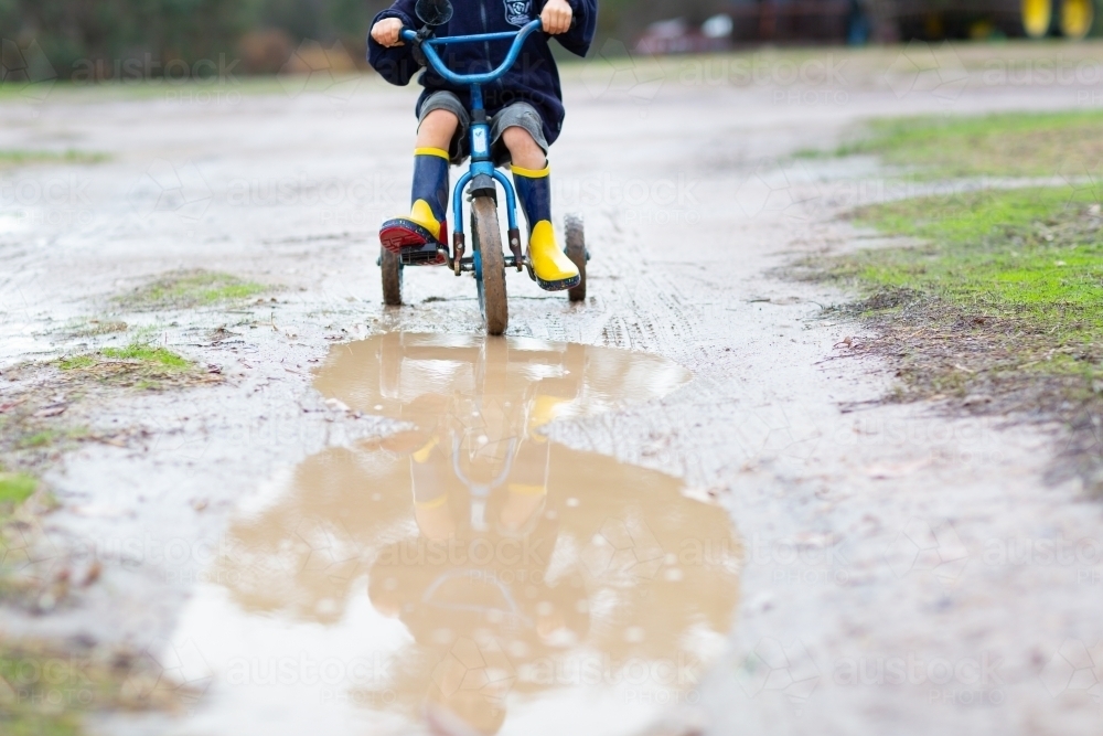 Child riding tricycle in puddles - Australian Stock Image