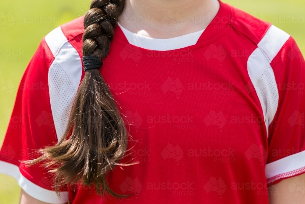 image-of-child-s-chest-in-red-sports-shirt-with-long-brown-hair-plait