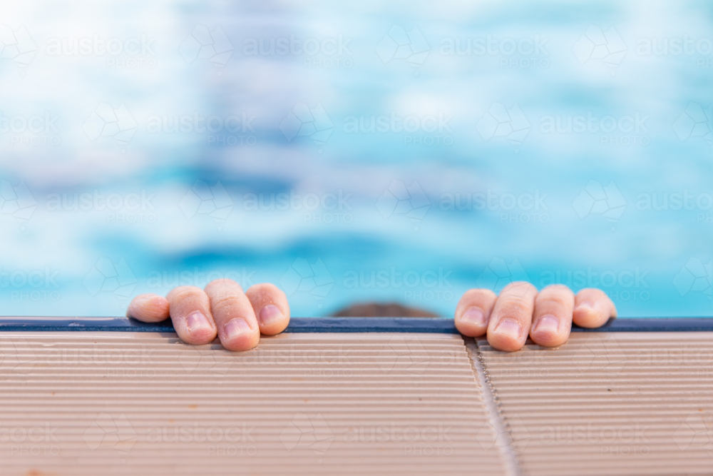 child's fingertips holding on to the edge of a public pool - Australian Stock Image