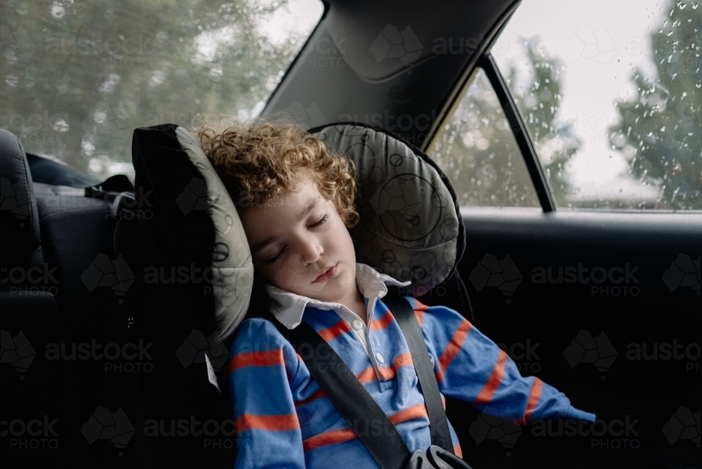 Child wearing a seat belt sleeping in the back seat of the family car - Australian Stock Image