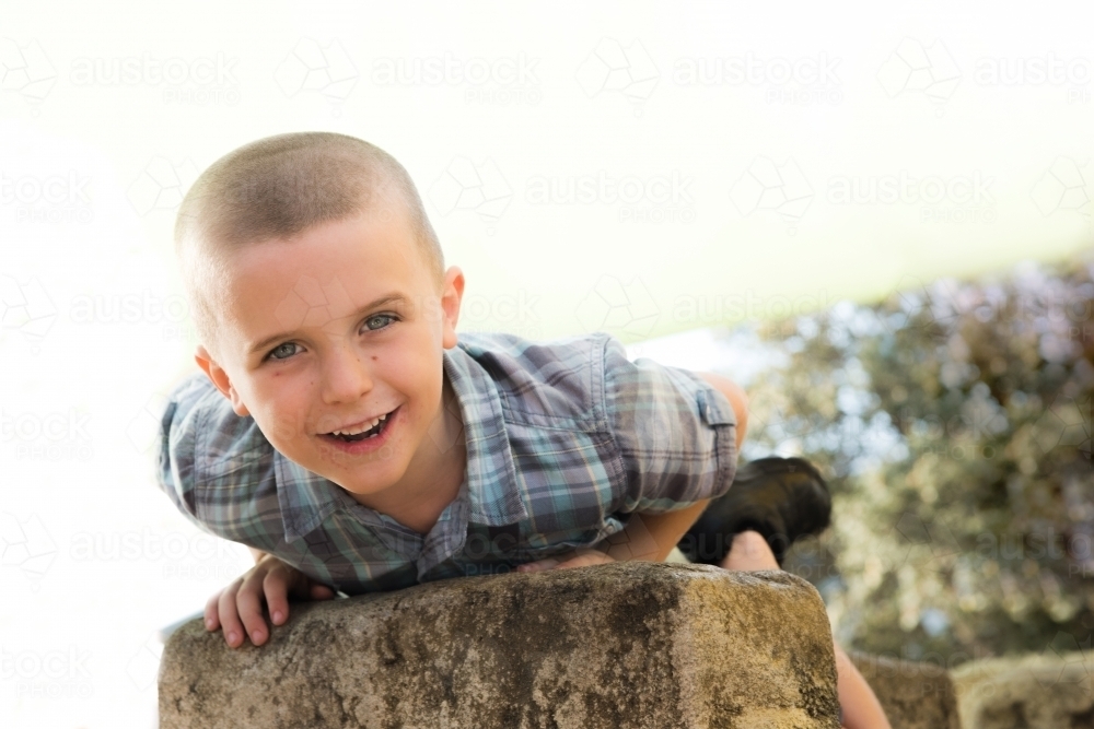 Child smiling at camera while laying on rock at park. - Australian Stock Image