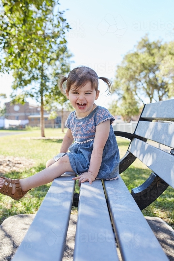 Child smiling on park bench wearing a blue dress - Australian Stock Image