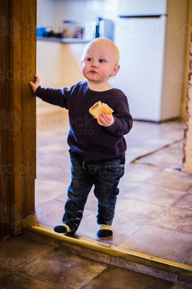 Child standing in doorway eating toast - Australian Stock Image