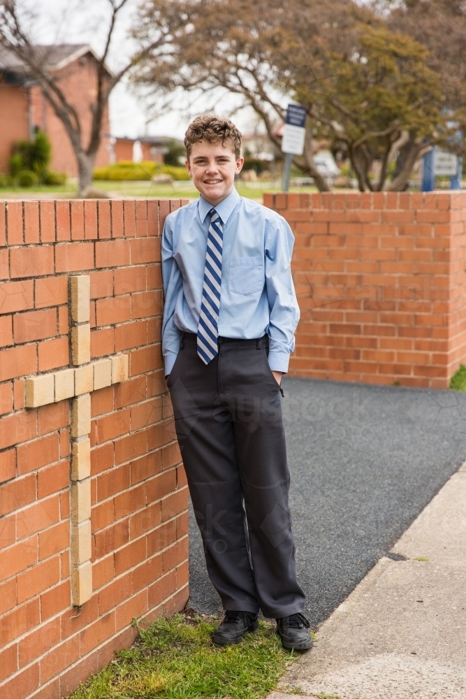 Child standing with hands in pockets leaning against brick entrance with cross to private school - Australian Stock Image