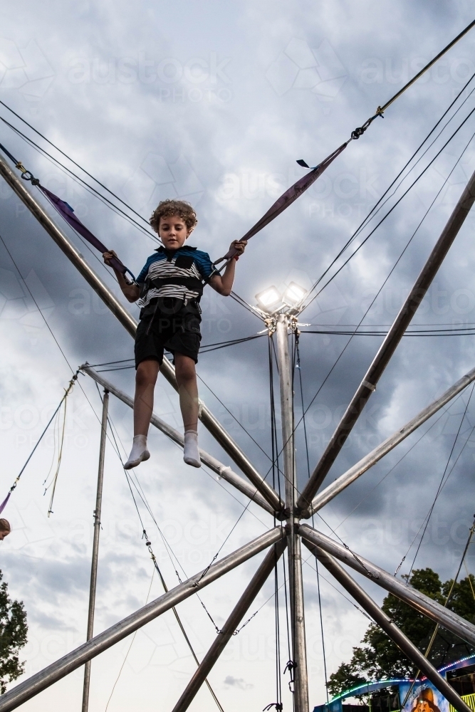 Child strapped into harness on ride at show, jumping in air - Australian Stock Image