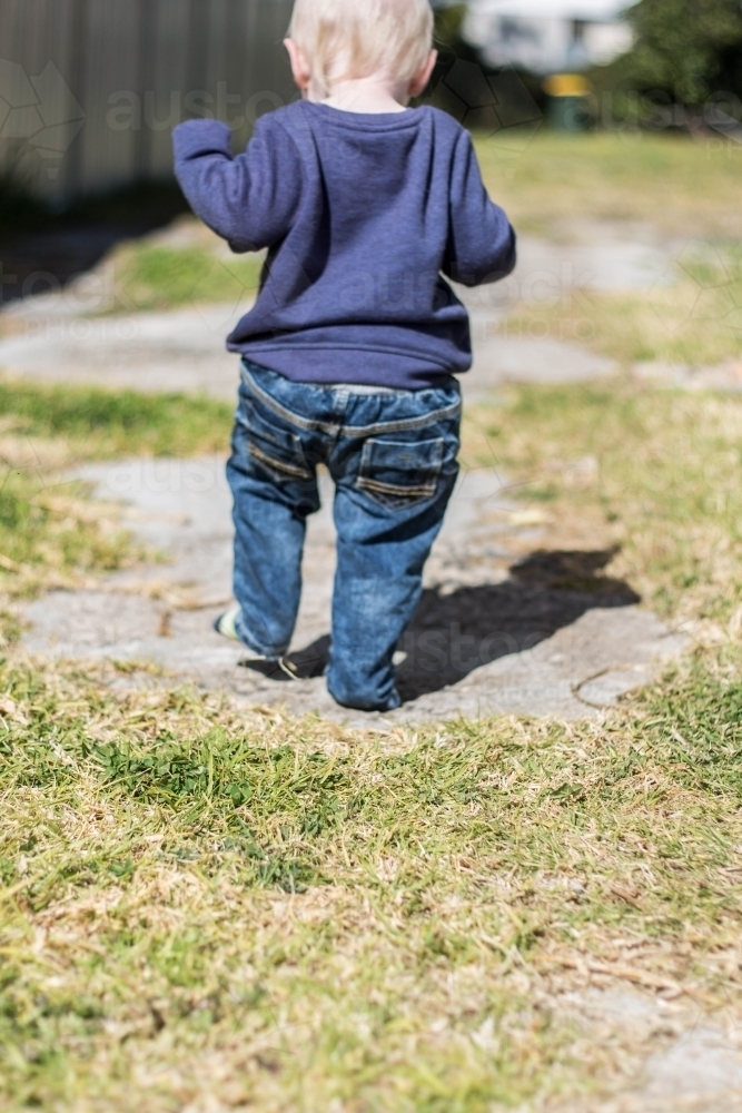 Child walking out of frame on patchy grass and concrete - Australian Stock Image