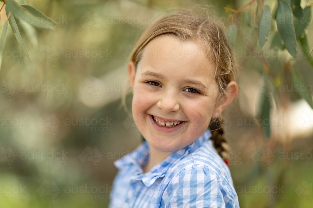 child with baby teeth smiling at camera with blurry leafy background - Australian Stock Image