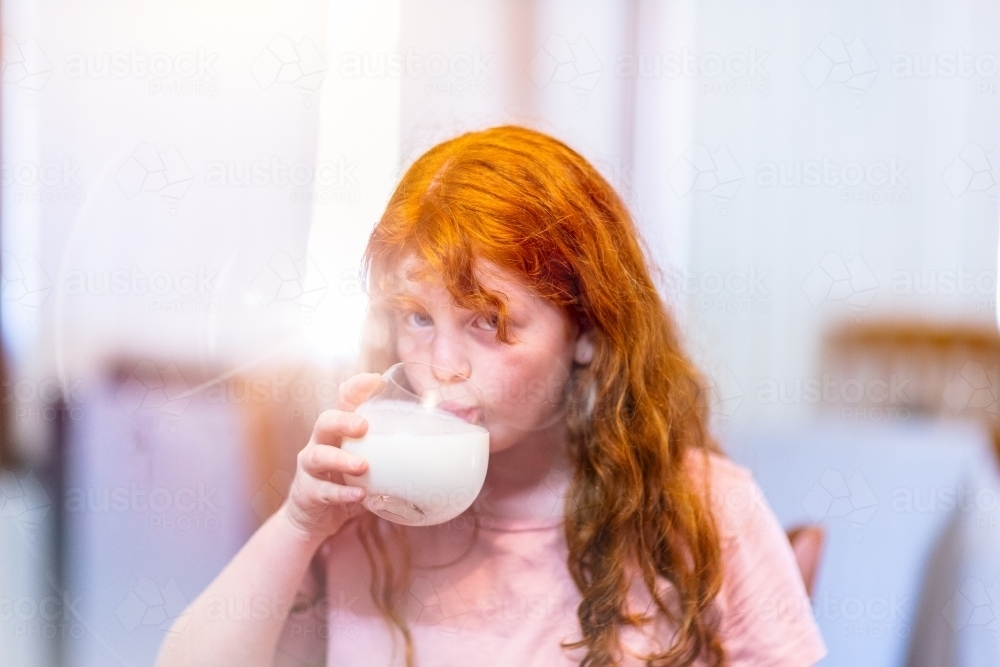 child with orange hair drinking milk from a glass - Australian Stock Image
