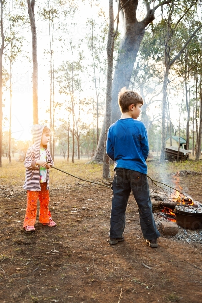 Children poking sticks into campfire at campsite - Australian Stock Image