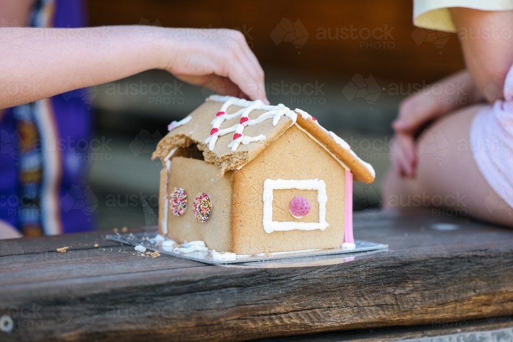 Children's hands pulling apart gingerbread house at Christmas time - Australian Stock Image