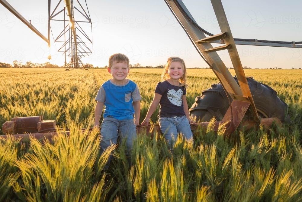 Children sitting on pivot irrigation system in wheat field paddock - Australian Stock Image