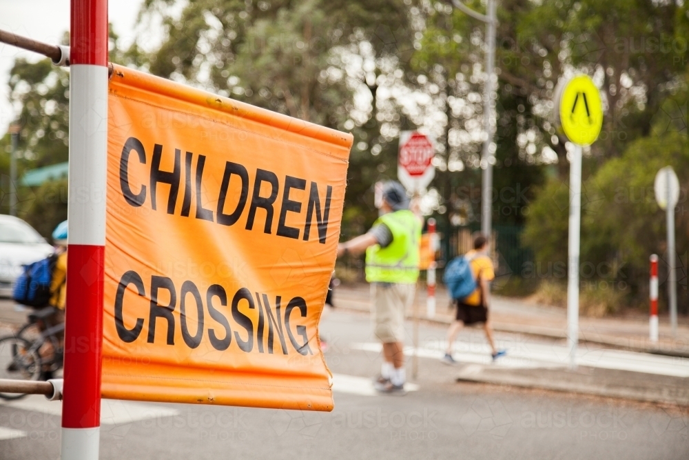 Children walking across pedestrian crossing with lollipop person - Australian Stock Image