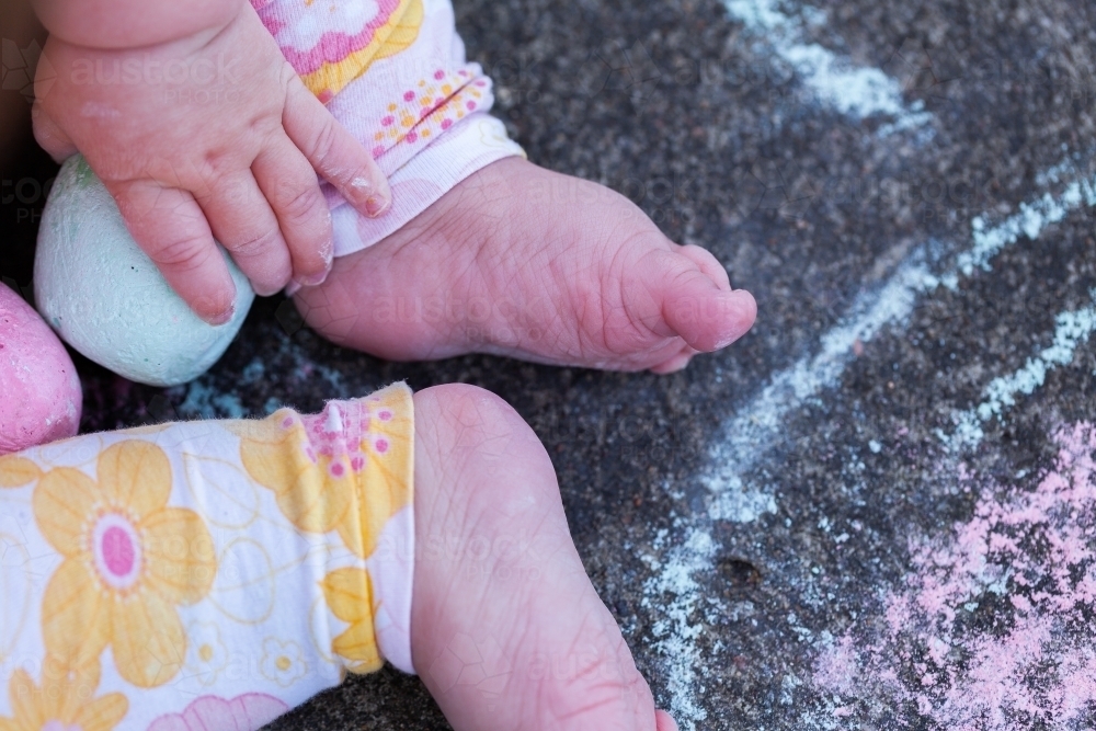 Chubby seven month old baby feet with chalk drawings on concrete - childhood - Australian Stock Image