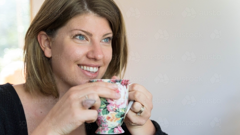 Close of young woman holding teacup looking away - Australian Stock Image
