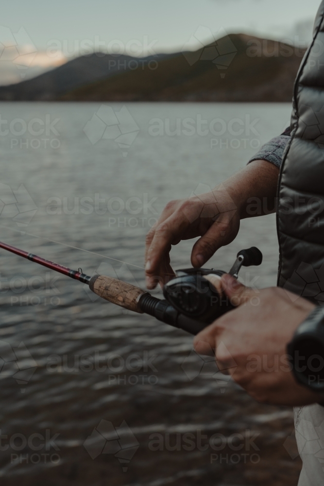 Close up detail shot of hands adjusting a reel while fishing - Australian Stock Image