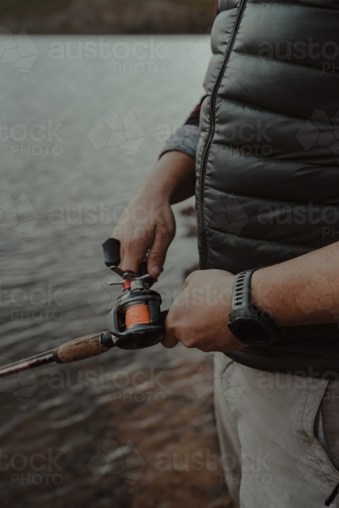 Close up detail shot of hands adjusting a reel while fishing - Australian Stock Image