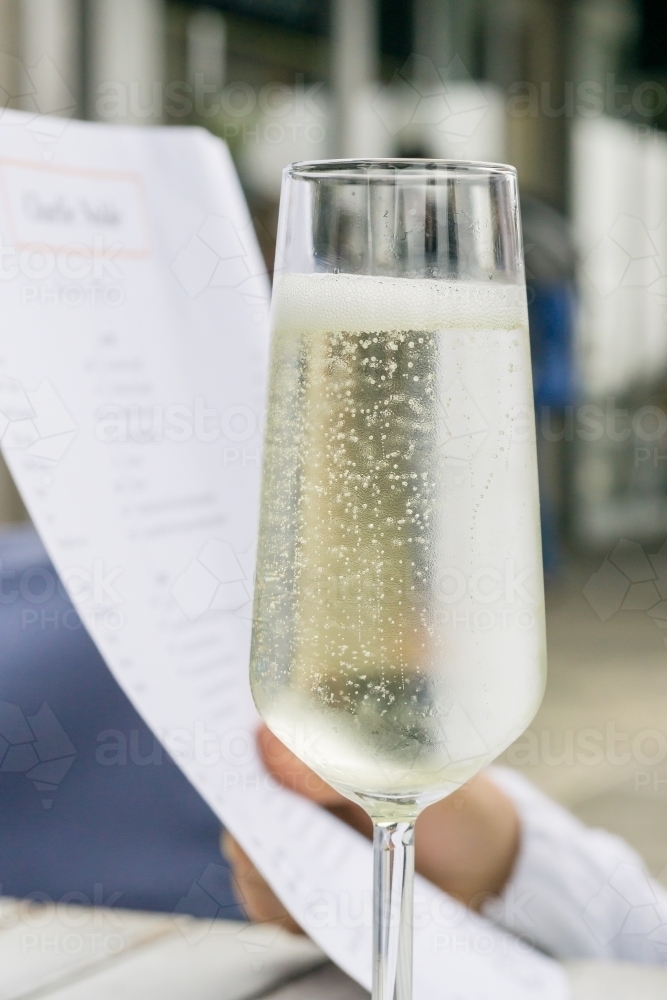 Close up of a glass of bubbly champagne with a menu being held behind - Australian Stock Image