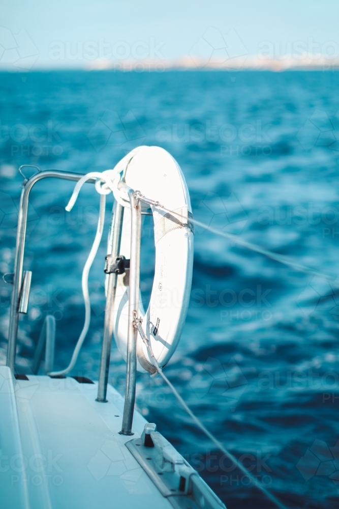 Close up of a life preserver attached to the wire railing of a boat on the water - Australian Stock Image