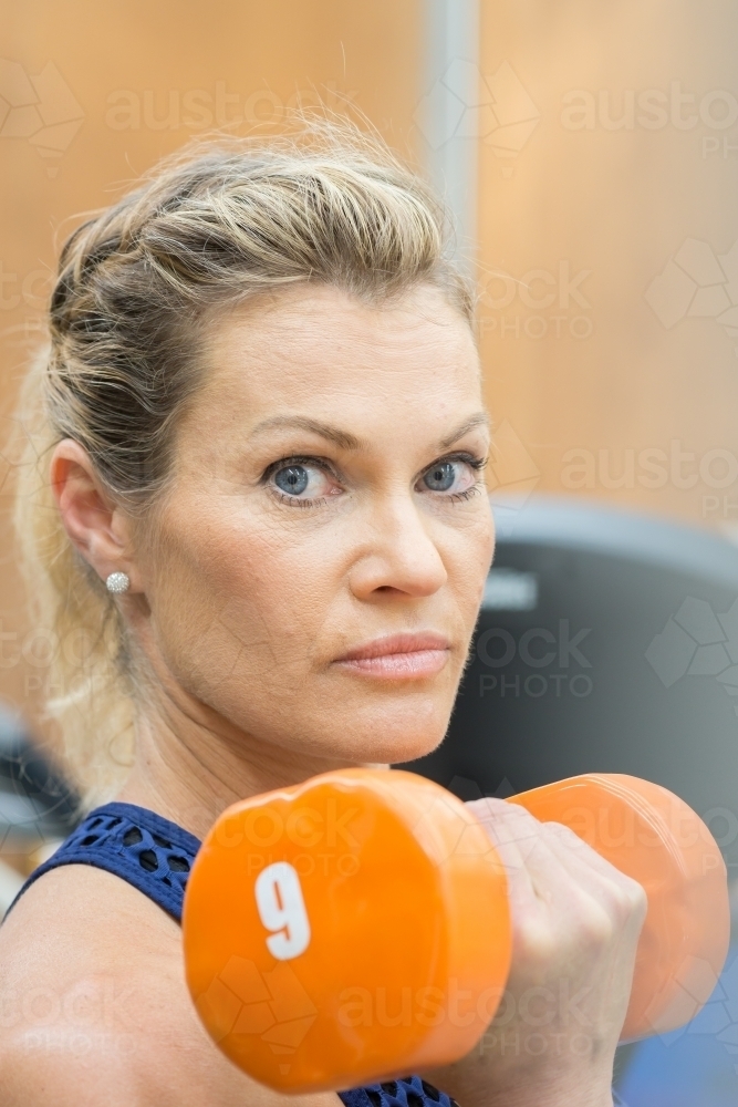 Close up of a woman lifting weights under her chin in a gym - Australian Stock Image