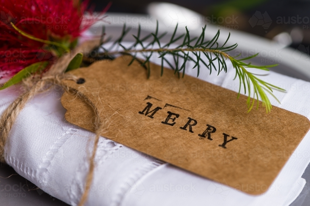 close up of a xmas tag with the word "merry" stamped in black ink on a plain tag - Australian Stock Image