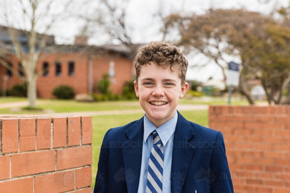 Close up of child in uniform smiling at school in front of buildings - Australian Stock Image