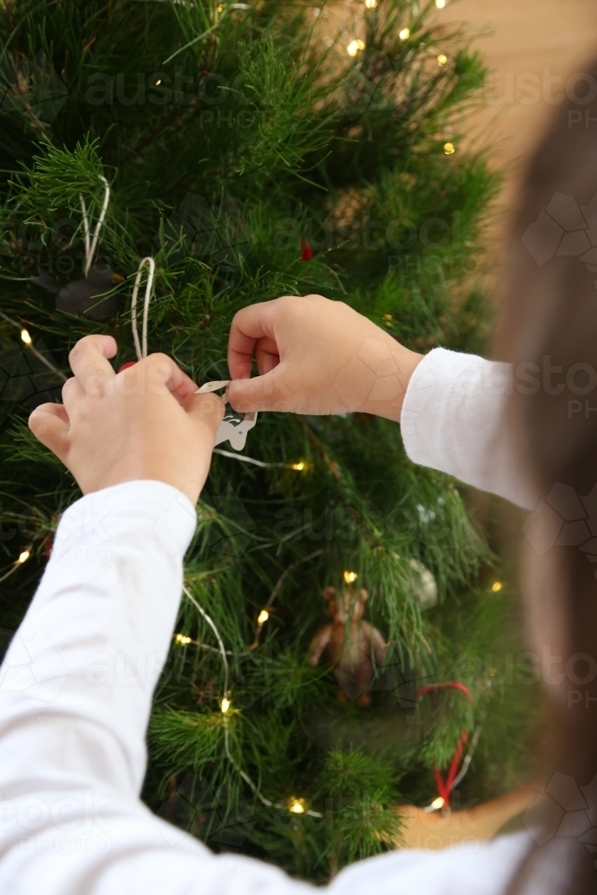 Close up of child's hands decorating Christmas tree - Australian Stock Image