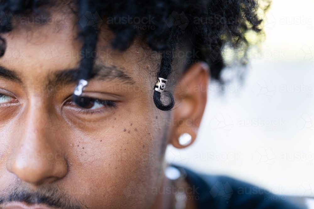 Close up of face of teenage boy with dark skin and beads in curly hair - Australian Stock Image