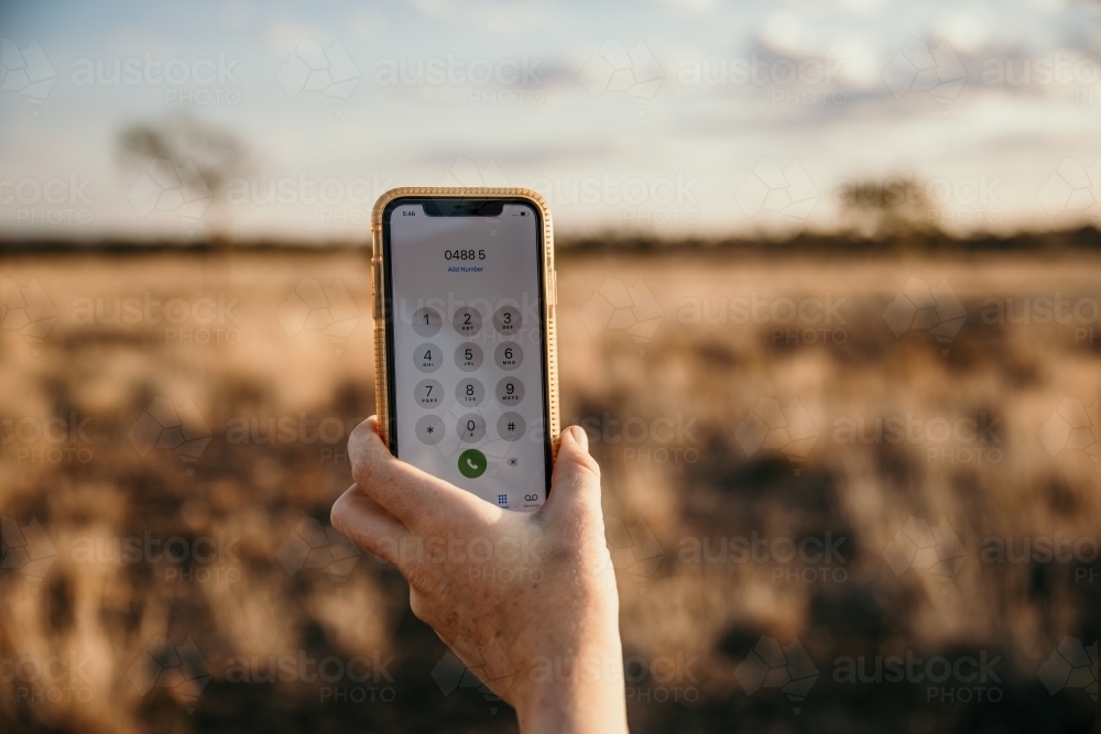 Close up of hand and smartphone in paddock - Australian Stock Image