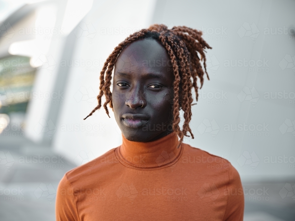 Close-up of South Sudanese man wearing orange turtleneck with urban background - Australian Stock Image