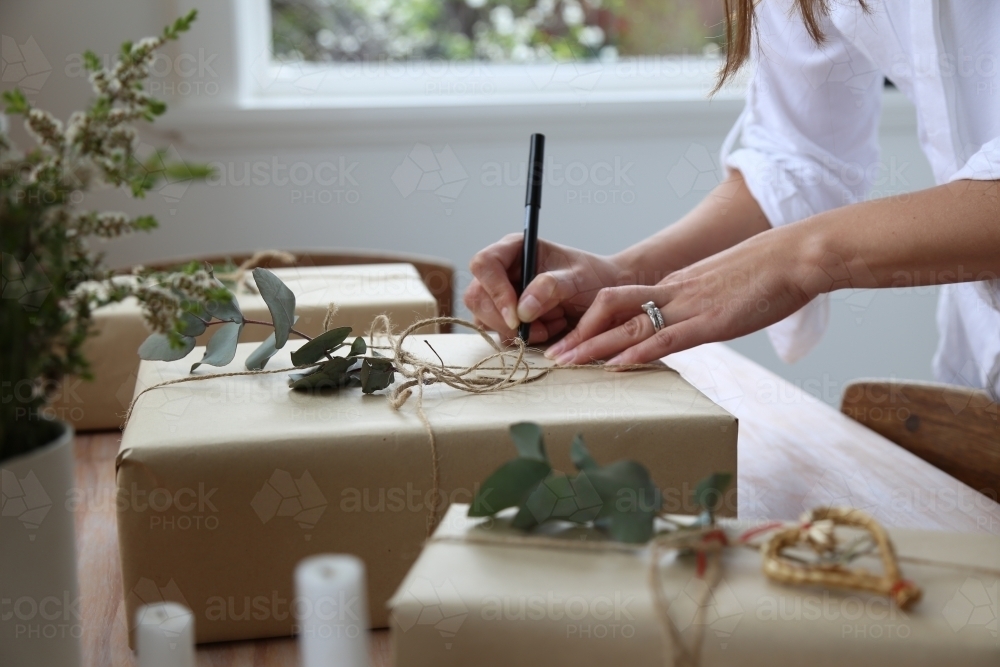 Close up of woman's hands writing gift tag for present - Australian Stock Image