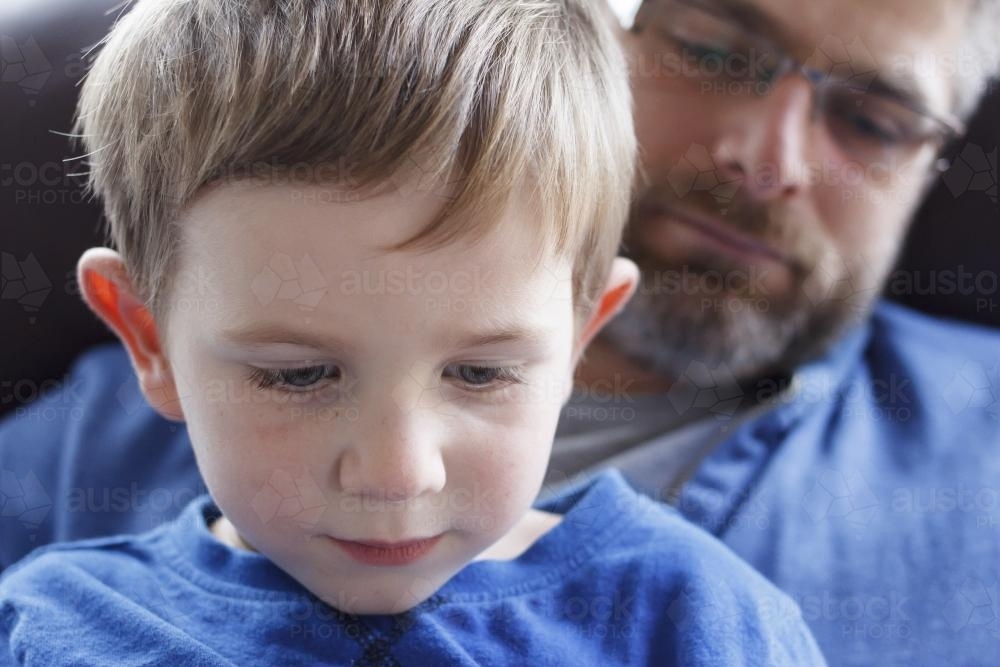 Close up of young boy sitting on dad's lap - Australian Stock Image