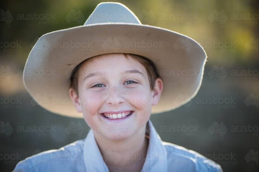 Close up of young boy smiling wearing akubra hat on farm in drought - Australian Stock Image