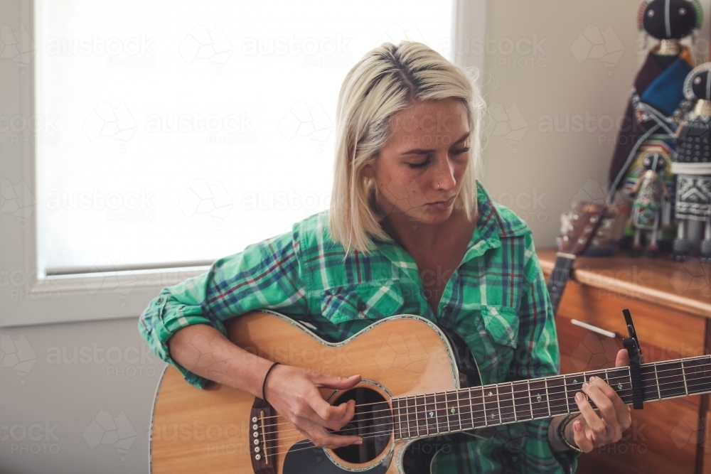 Close up of young woman looking down as she plays the guitar - Australian Stock Image