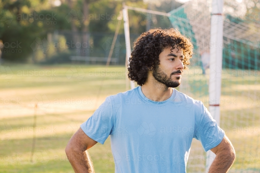 Close up photo of a man with curly hair with beard wearing blue shirt with arms against the hips - Australian Stock Image