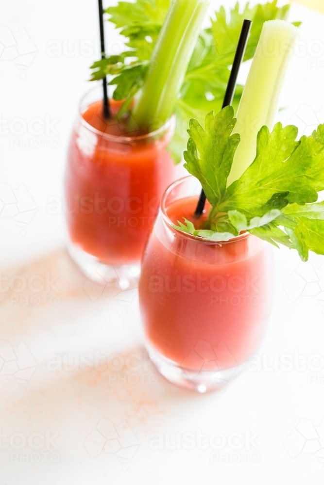 Close up photo of a red beverage with chopped celery in a glass cup with a black straw - Australian Stock Image