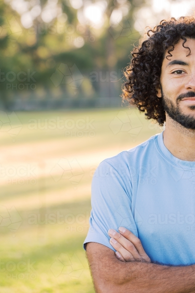 Close up photo of a smiling man with curly hair with beard wearing blue shirt on a sunny day - Australian Stock Image