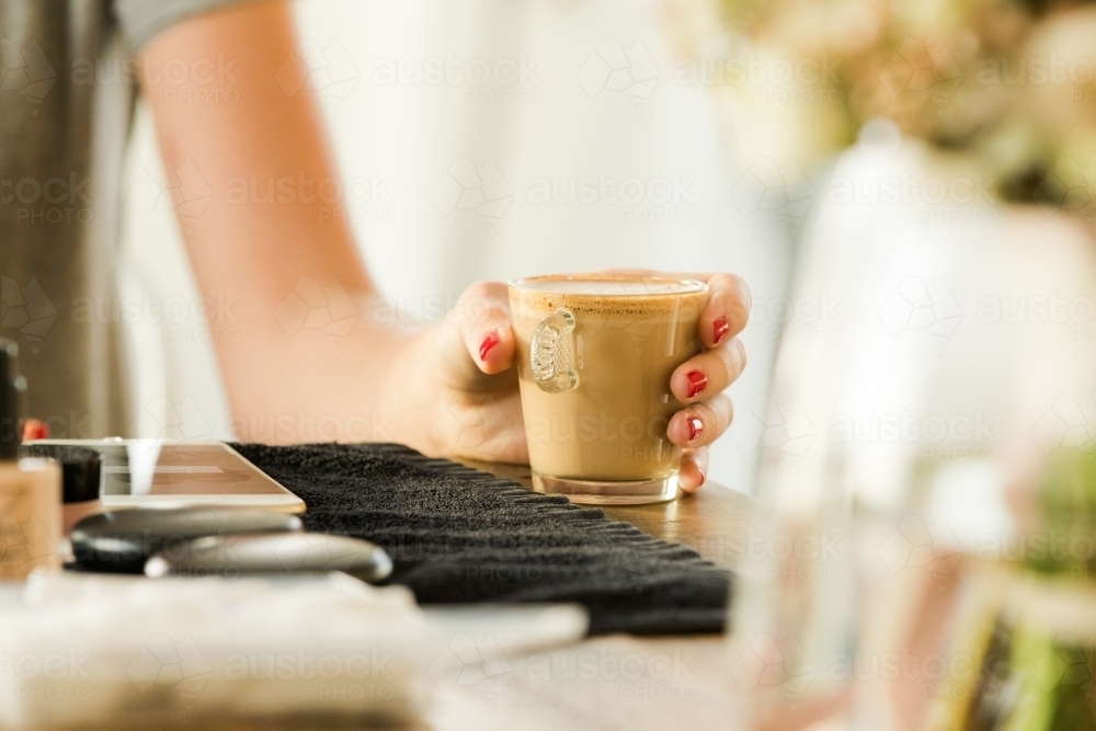 Close up photo of woman's arm with red nails holding a cup of coffee - Australian Stock Image