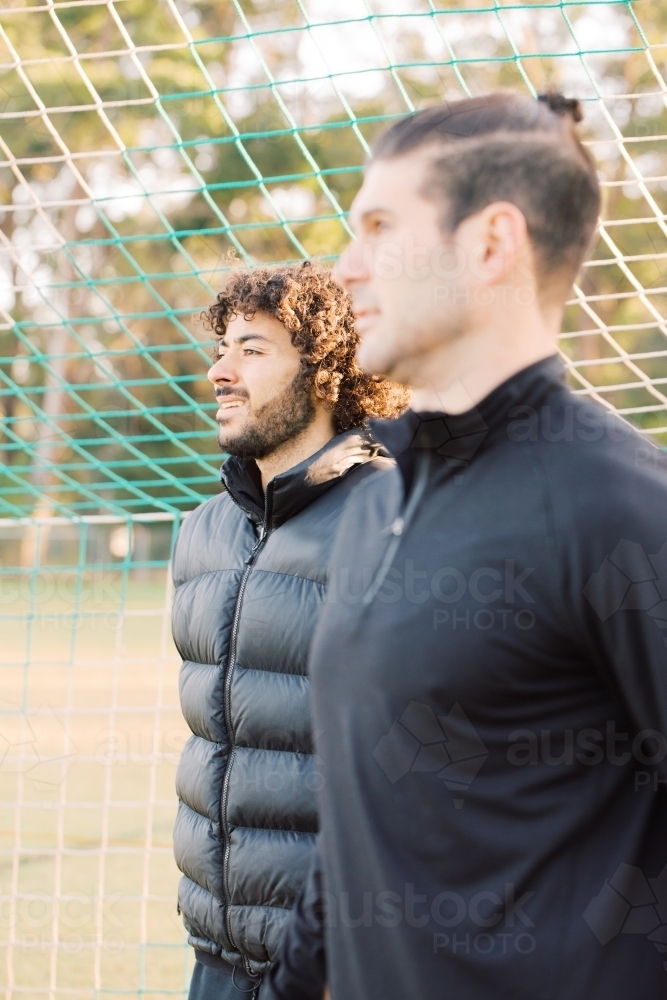 Close up photo of young interracial men standing on the field looking a far near the soccer net - Australian Stock Image