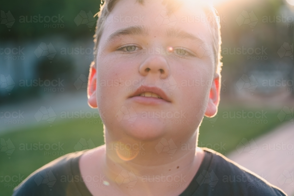 Close up portrait image of pre-teen boy in golden afternoon sun with lens flare - Australian Stock Image