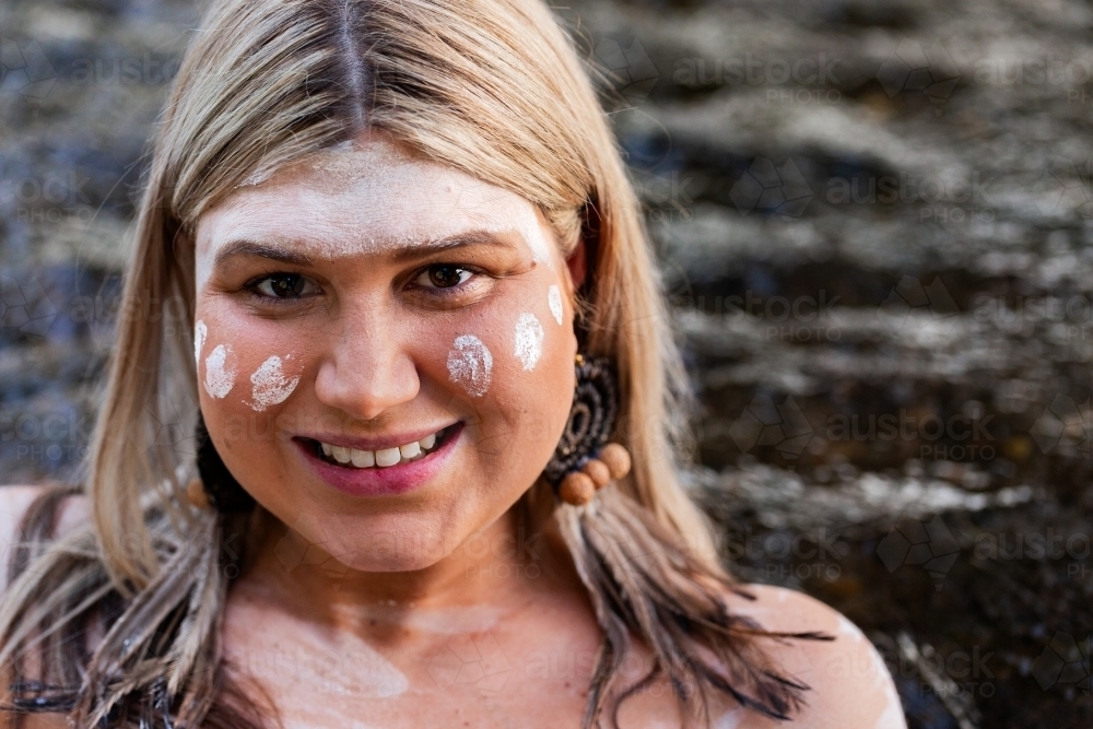 Close up portrait of aboriginal woman smiling with woven earring and ochre paint on face - Australian Stock Image