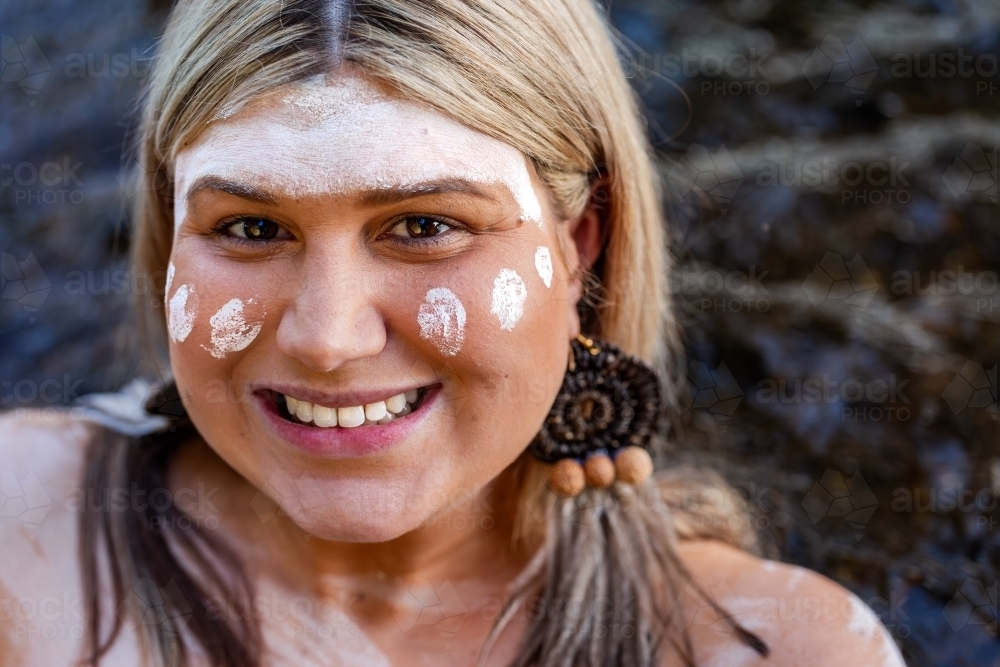 Close up portrait of aboriginal woman with woven earring and ochre paint on face - Australian Stock Image