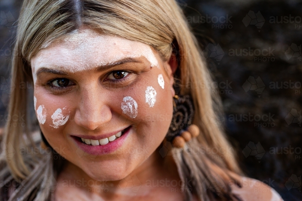 Close up portrait of aboriginal woman with woven earring and ochre paint on face - Australian Stock Image