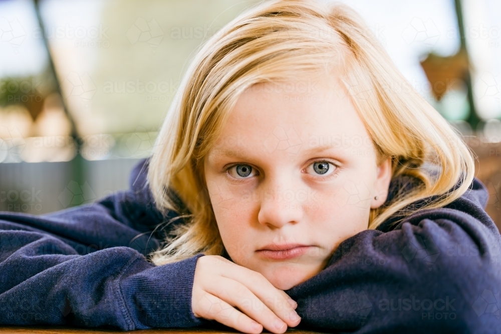 Close up portrait of pre-teen boy with long blonde hair and blue eyes. Resting chin on hands - Australian Stock Image