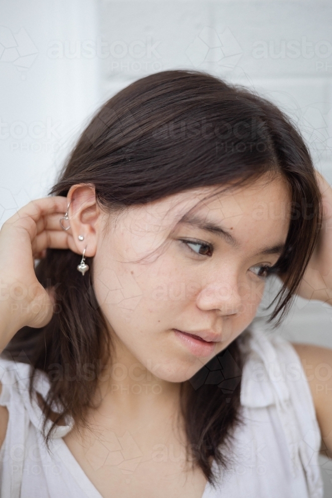 Close-up portrait of teenage girl pushing hair behind ear - Australian Stock Image