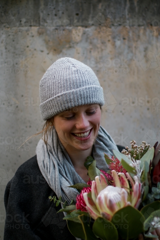 Close up portrait of young girl wearing a beanie and scarf smiling whilst holding a floral bouquet - Australian Stock Image