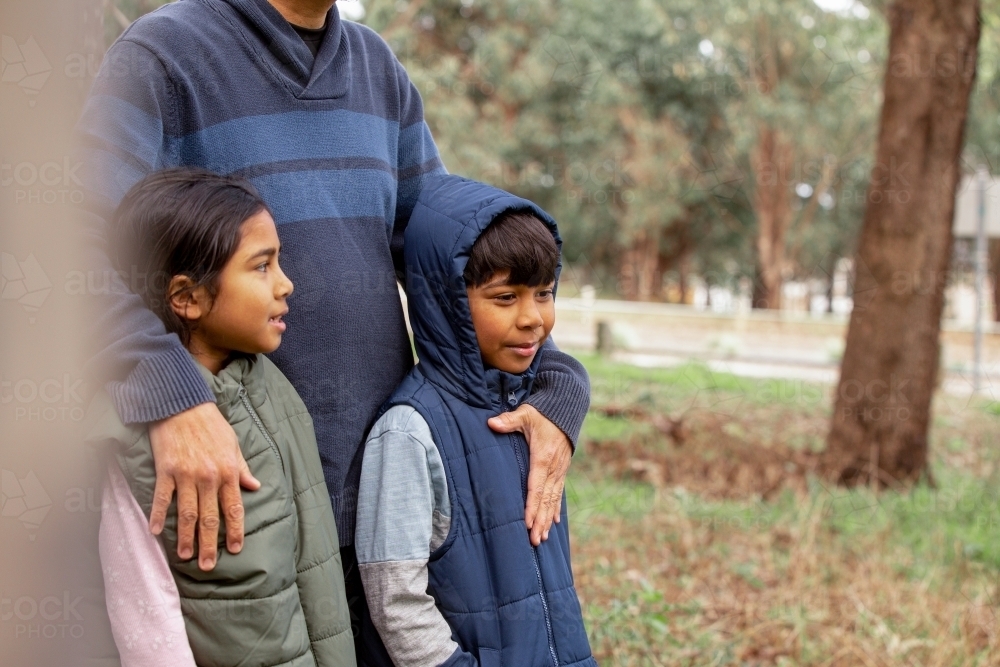 Close up shot of a boy wearing blue coat and a girl wearing green coat being held by man on a field - Australian Stock Image